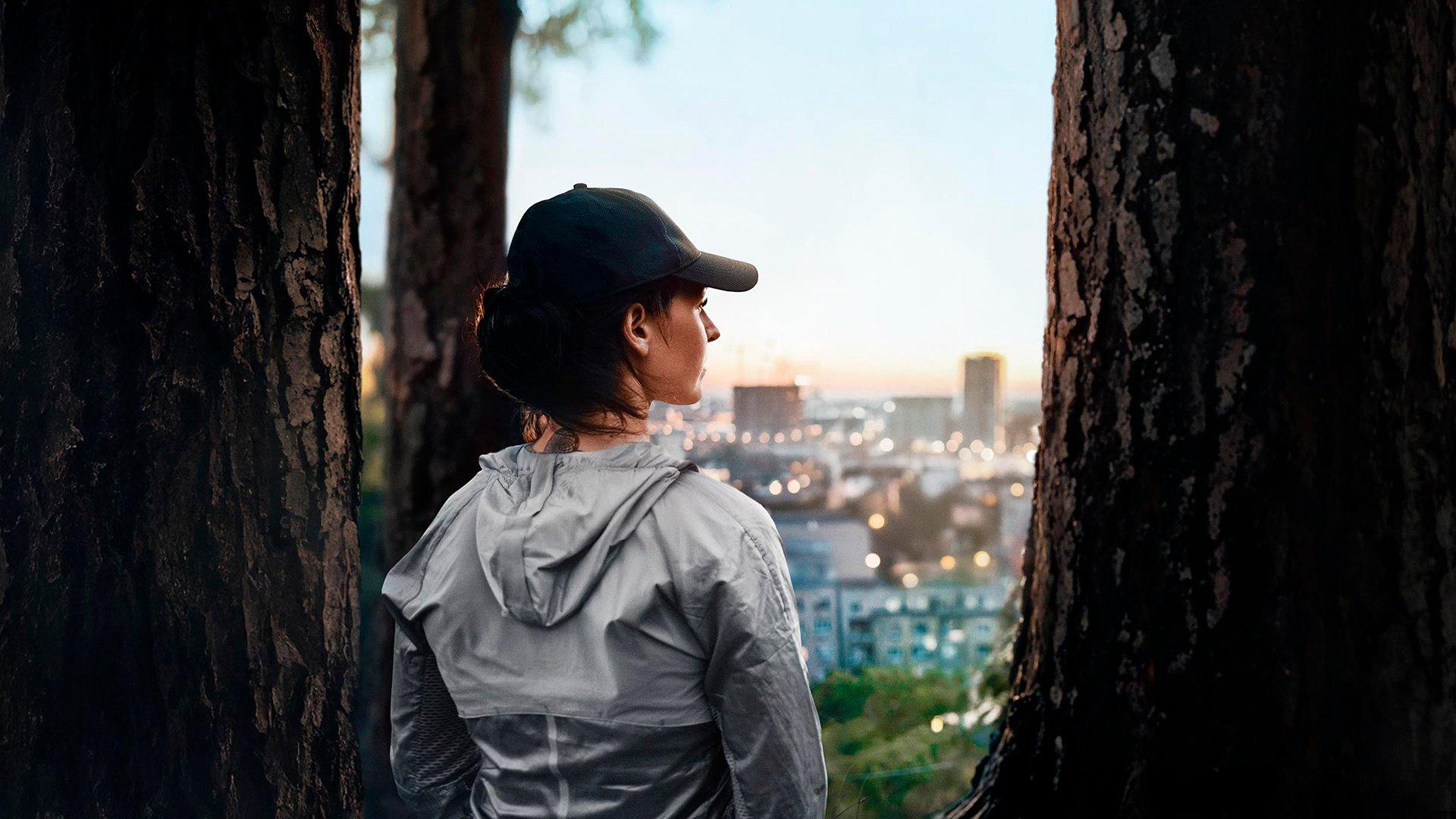 Person standing between trees, overlooking a cityscape at sunset.